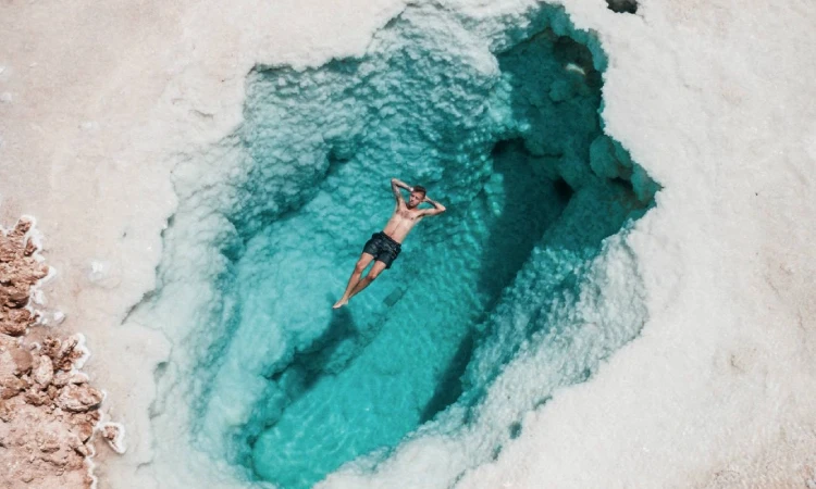 A breathtaking view of Siwa Oasis in Egypt showing turquoise salt lakes, palm trees, and golden desert dunes under a clear blue sky.